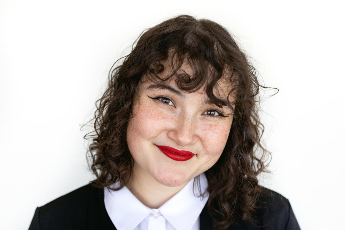 Portrait of Jimena Jimenez who has dark brown wavy hair, who is wearing a white collared shirt with a black cardigan on top.